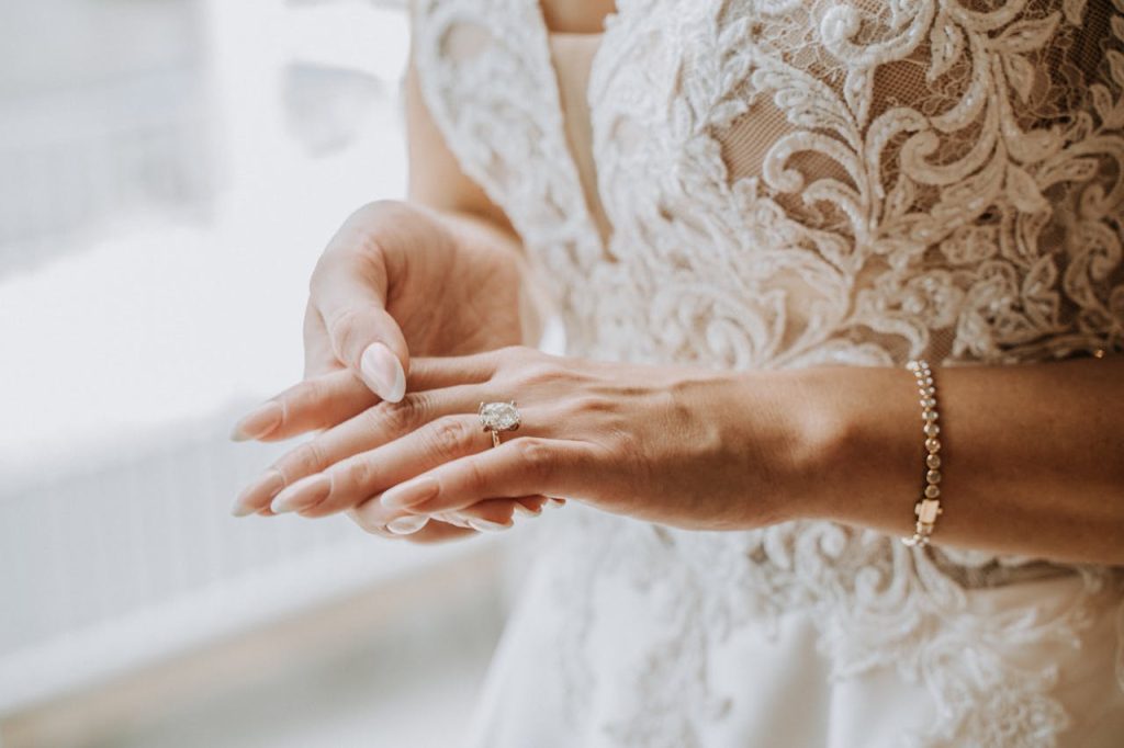 Close-up of a bride adjusting her wedding ring, showcasing elegant jewelry and embroidery.