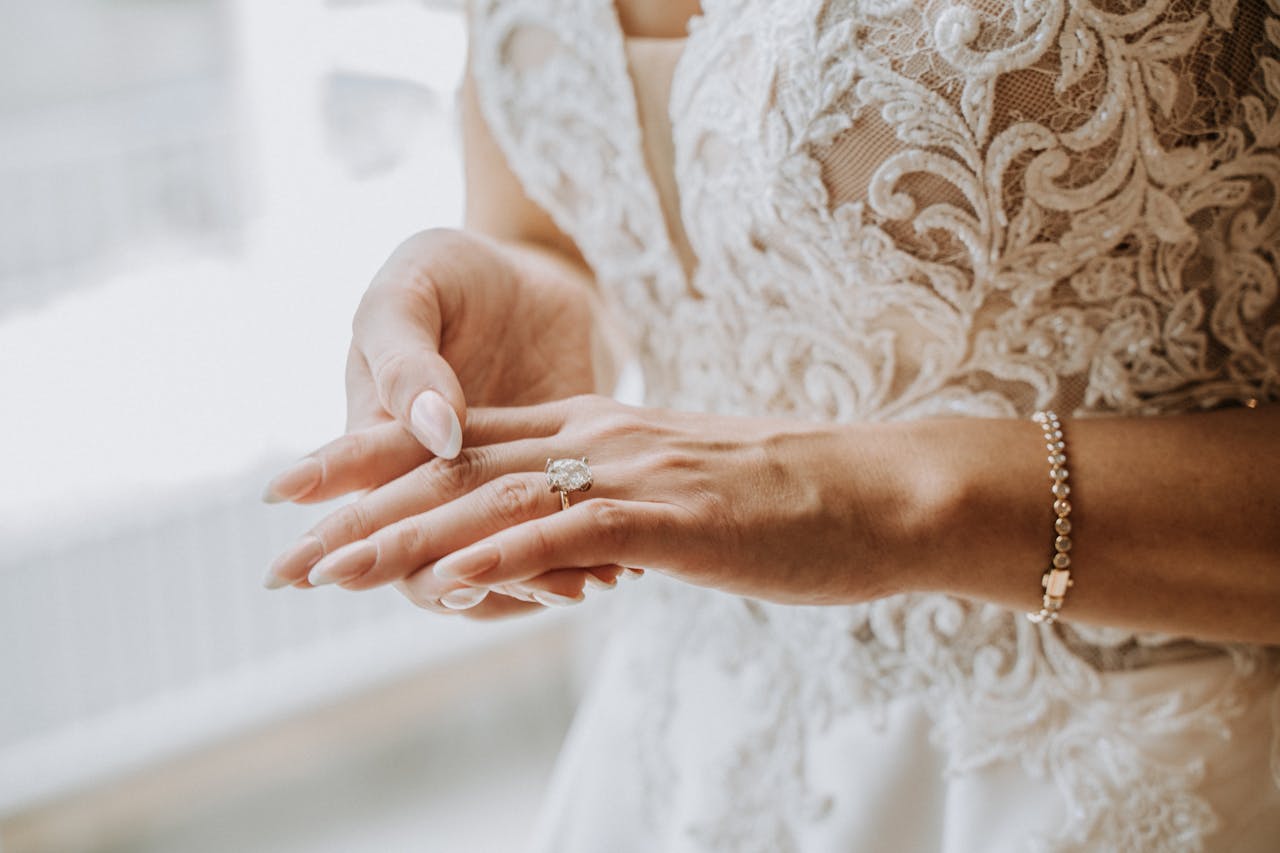 Close-up of a bride adjusting her wedding ring, showcasing elegant jewelry and embroidery.